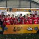 "Foto da equipe de futebol Sub-10 da Escola Rubra de Pontal do Paraná posando com o troféu de campeão. Os jovens atletas e a comissão técnica sorriem para a câmera, exibindo suas medalhas douradas em frente ao banner do evento Gol de Placa Cup."