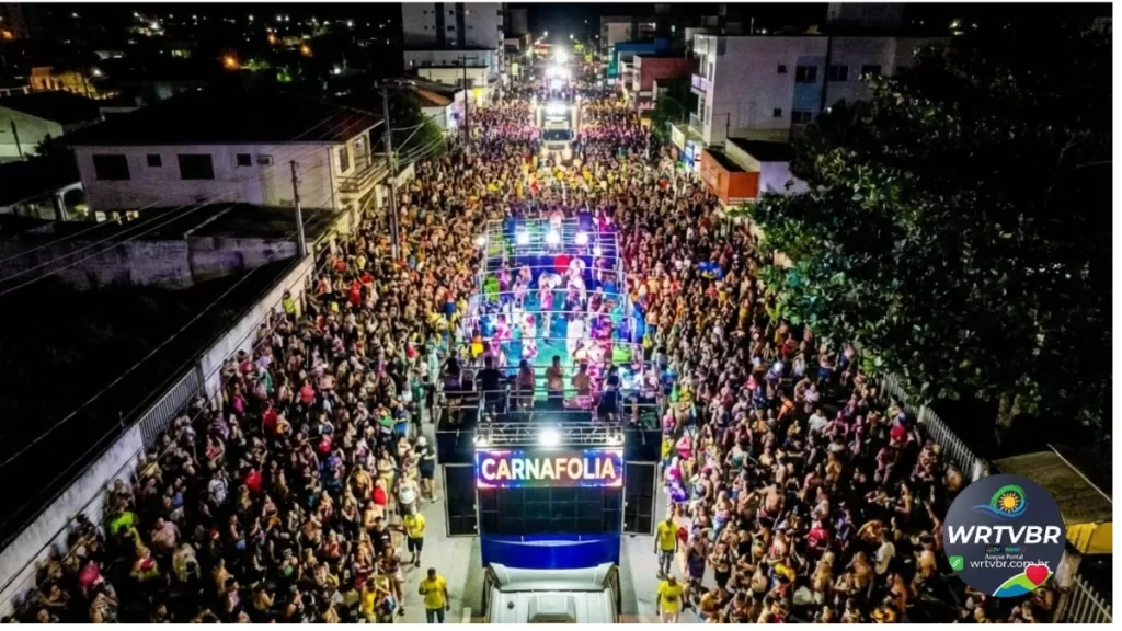 Vista aérea de uma multidão acompanhando o trio elétrico iluminado durante o Carnaval em Pontal do Paraná.