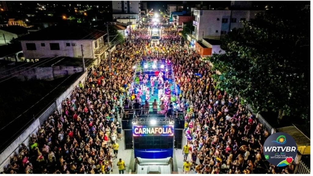 Vista aérea de uma multidão acompanhando o trio elétrico iluminado durante o Carnaval em Pontal do Paraná.