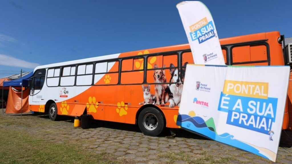 Ônibus laranja da Unidade Móvel de Castração de Pontal do Paraná estacionado em área gramada com placas informativas da prefeitura ao lado.